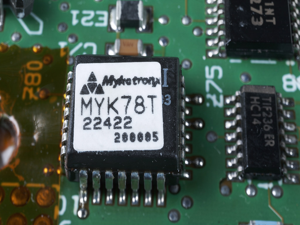 A half-inch square black chip soldered to a green circuit board, its white label reading Mykotronx, MYK78T, 22422, 288885, surrounded by ordinary logic chips.